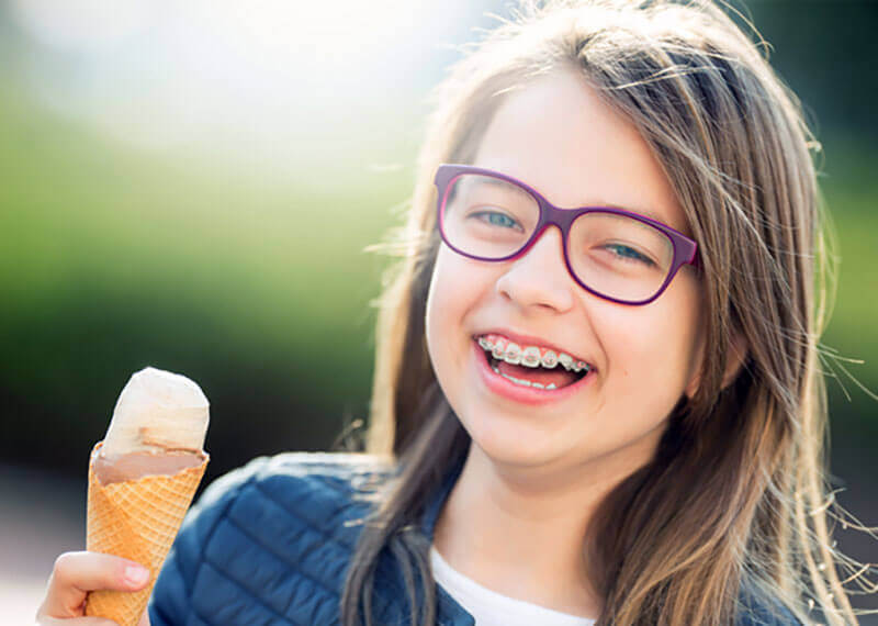 smiling girl with braces and glasses holding an ice cream cone